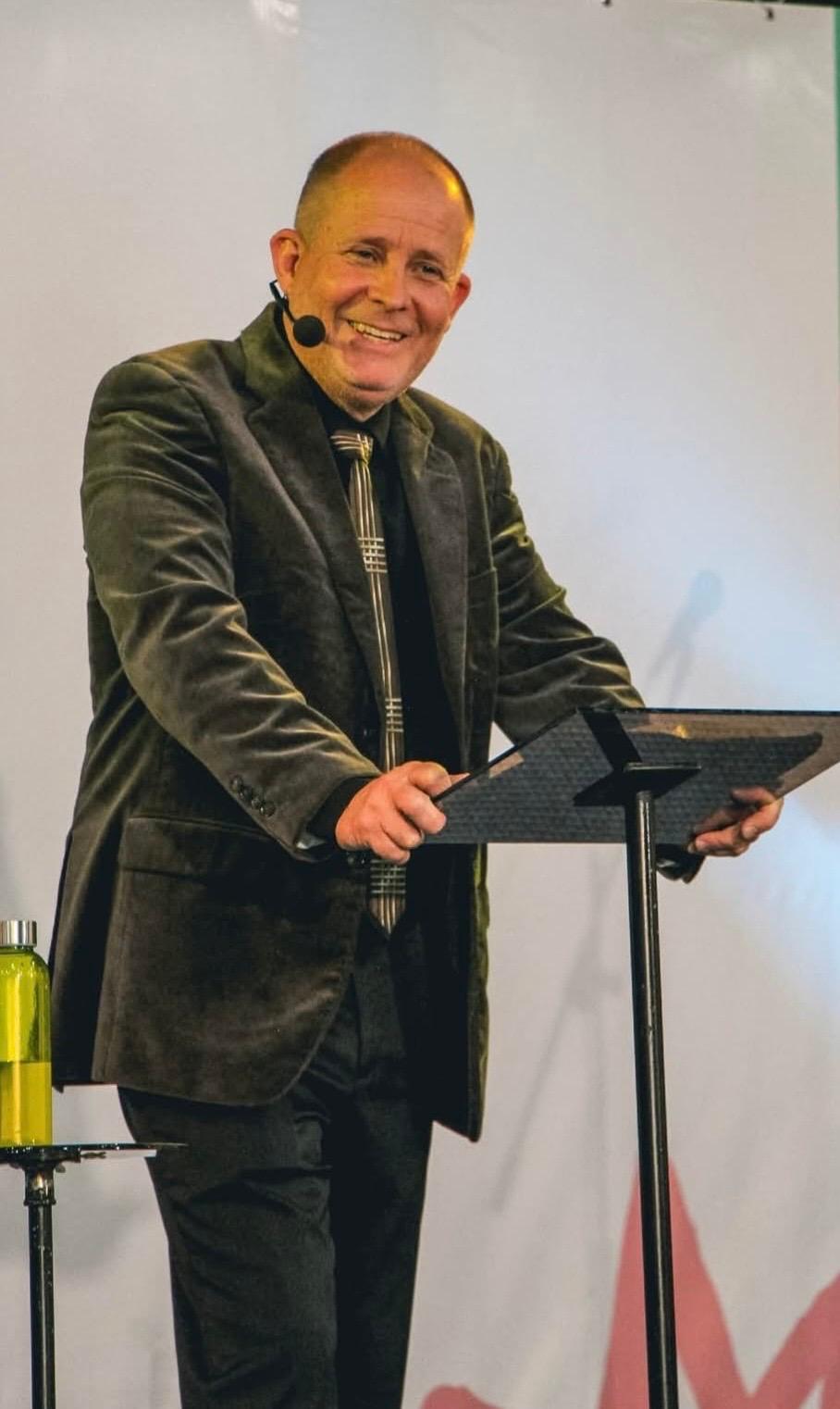 David Larson at the pulpit smiling mid-message
