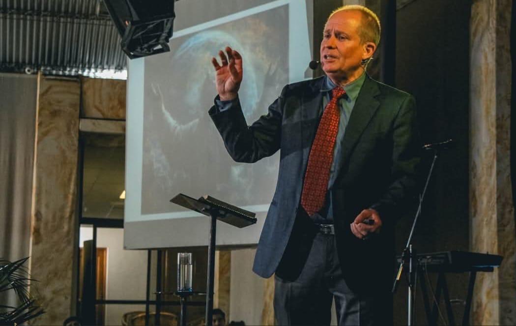 David Larson preaching with world projection behind him